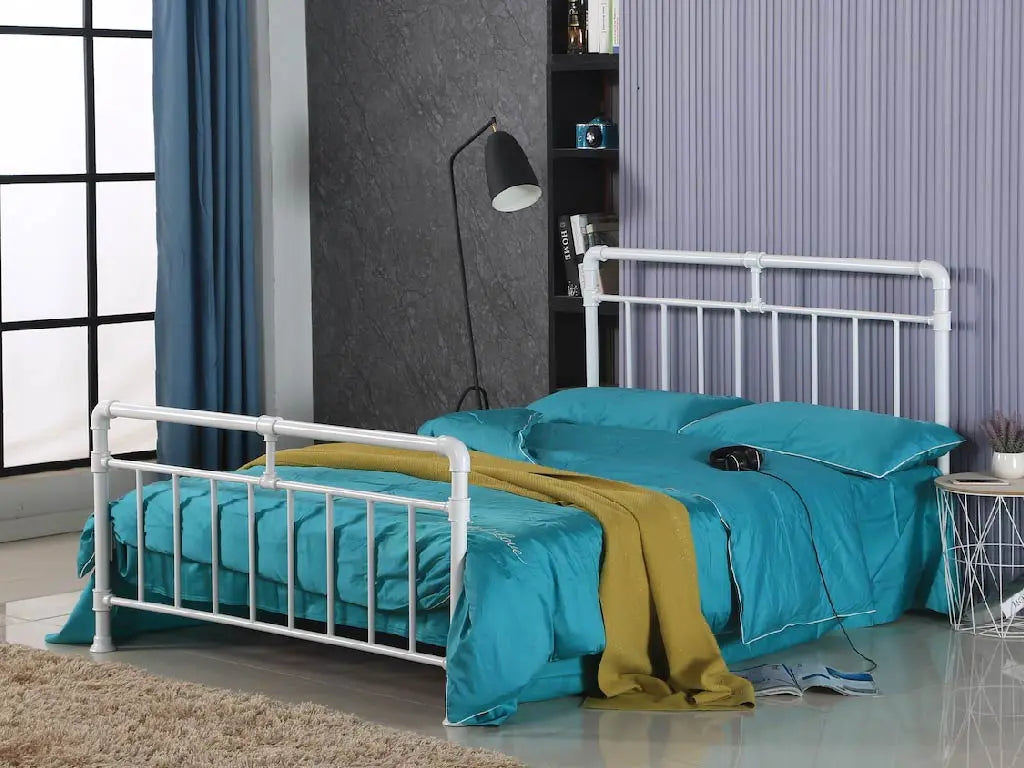 White metal bed frame with turquoise bedding and yellow blanket in a room with striped wallpaper. | White